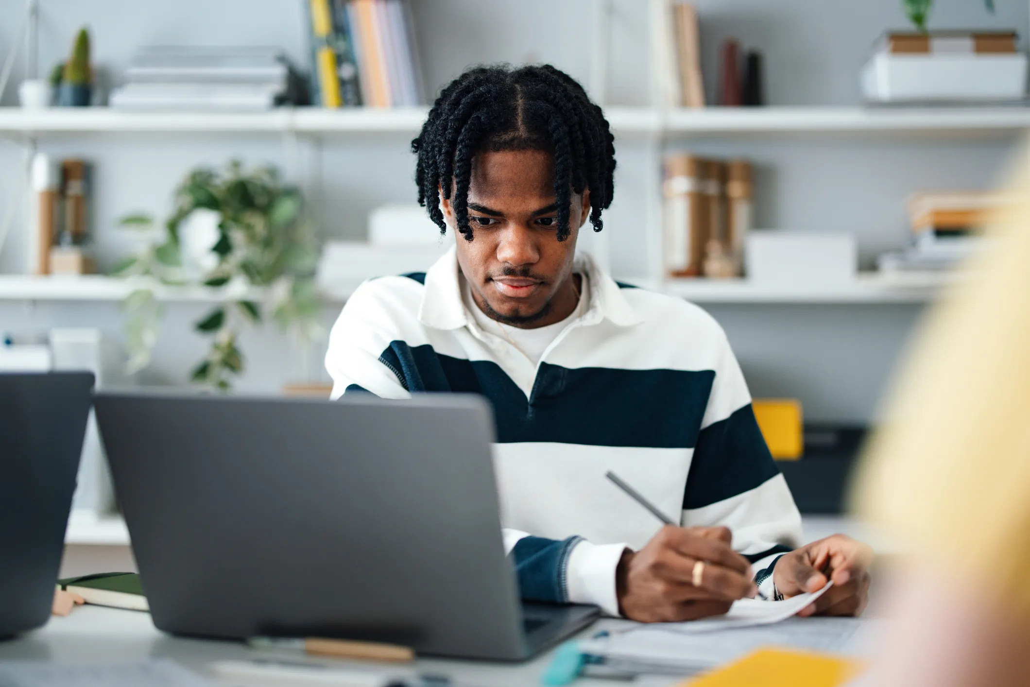 A young professional studies at a desk with a laptop and notebook, focused on preparing for upcoming job interviews.