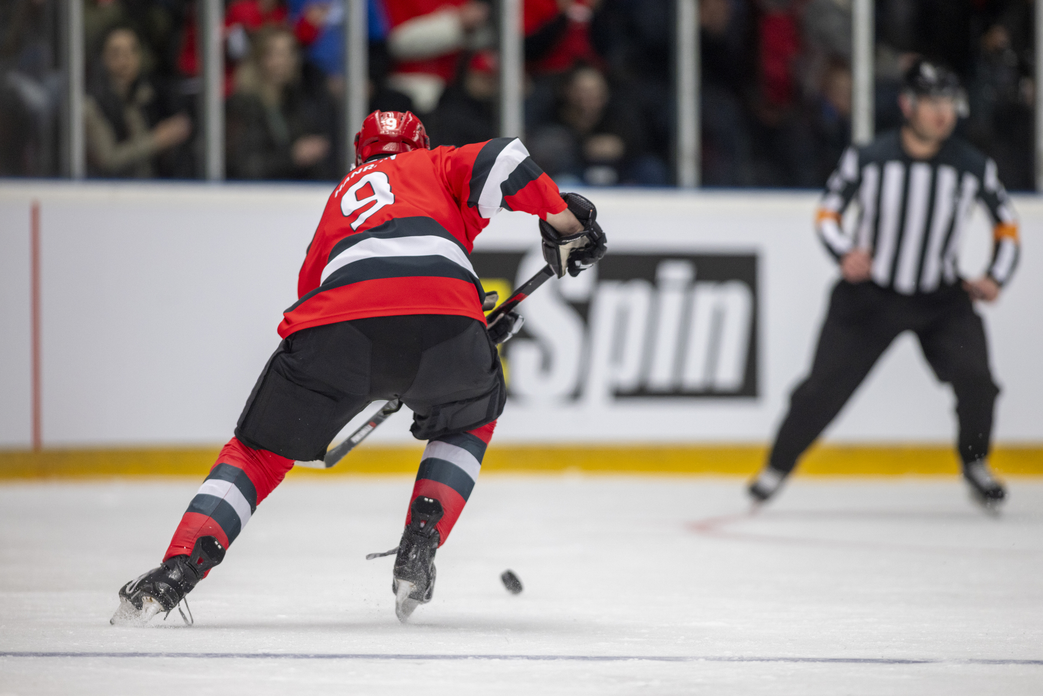 A male ice hockey player in a red jersey with the number 9 skates towards the puck