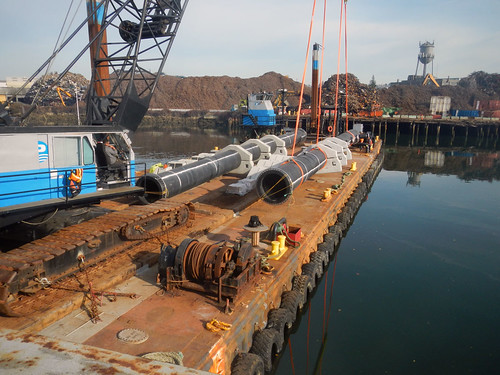 Barge docked at water with industrial pipes and crane equipment on board in a harbor.