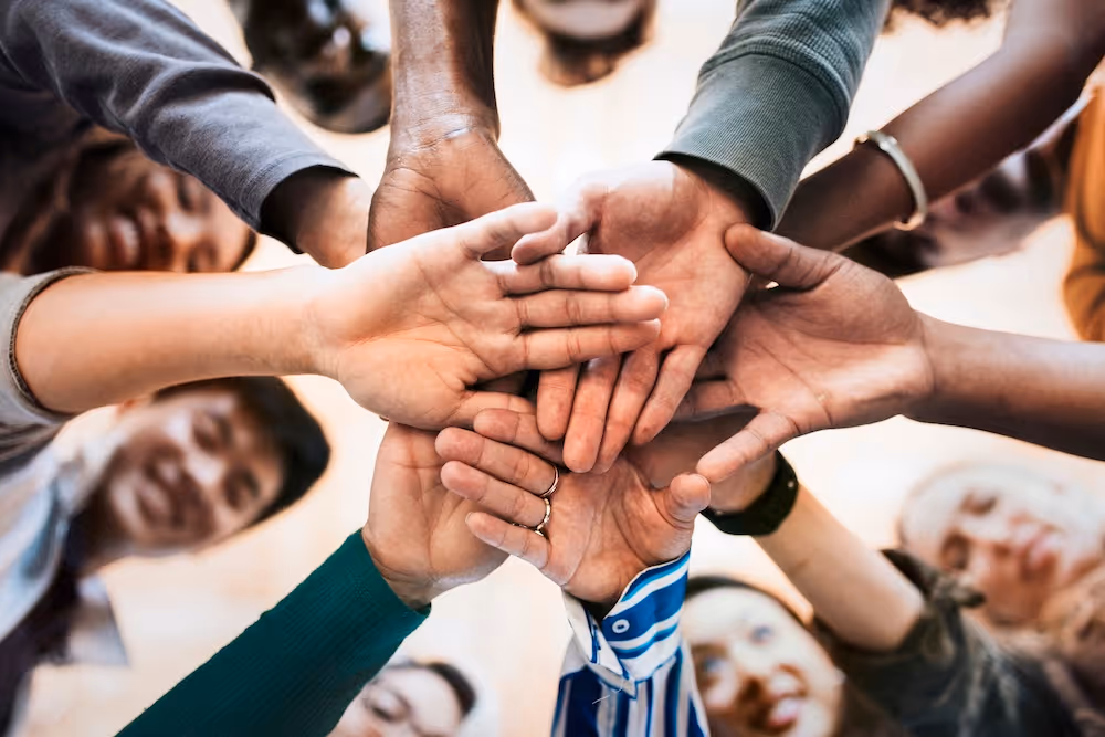 Diverse group of people standing in a circle with their hands stacked together in the center.