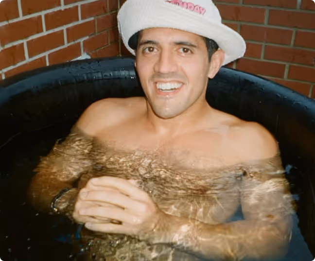 Ben wearing a white hat sitting in a tub of water against a brick wall background.