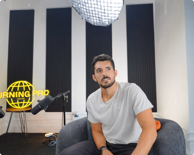 Ben sitting in a gray chair in a recording studio with a microphone and a glowing yellow 'TURNING PRO' sign in the background.