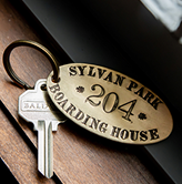 Metal keyring with an oval brass tag reading 'Sylvan Park 204 Boarding House' attached to a silver key.