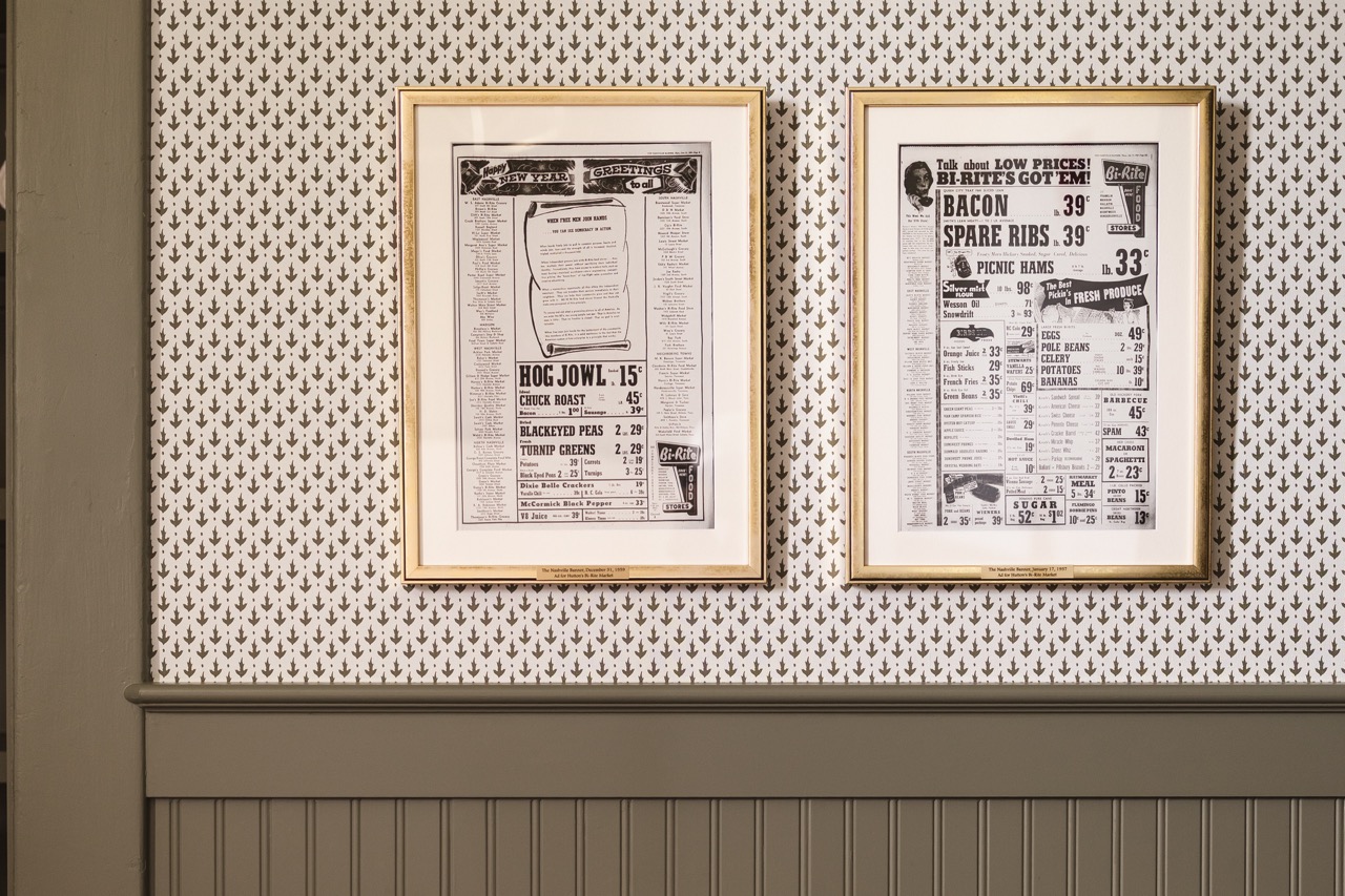 Two framed vintage newspaper advertisements with prices for meat and groceries on patterned wallpaper.