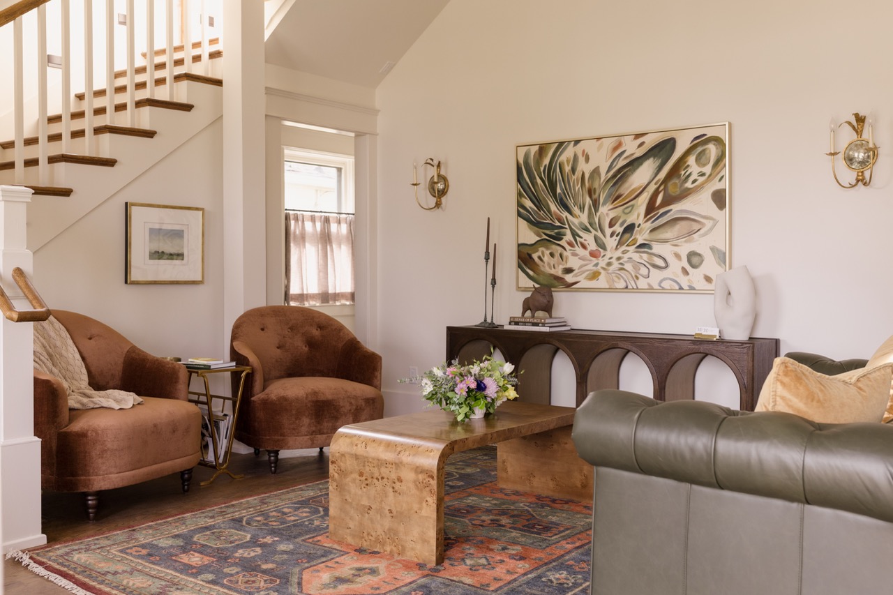 Living room with brown velvet chairs, wooden coffee table with flowers, green leather sofa, and abstract wall art.