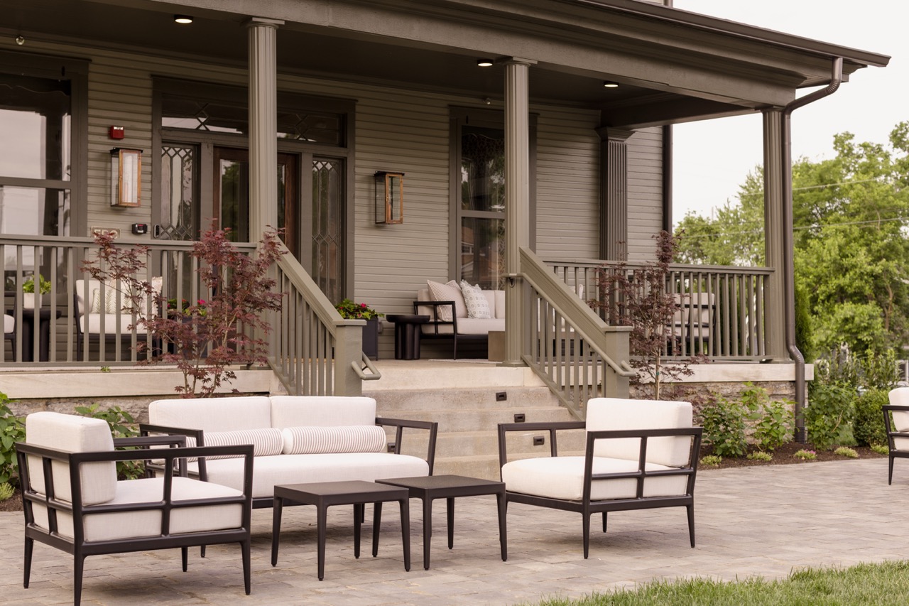 Modern porch with beige cushioned outdoor chairs and a small black table on a stone patio.