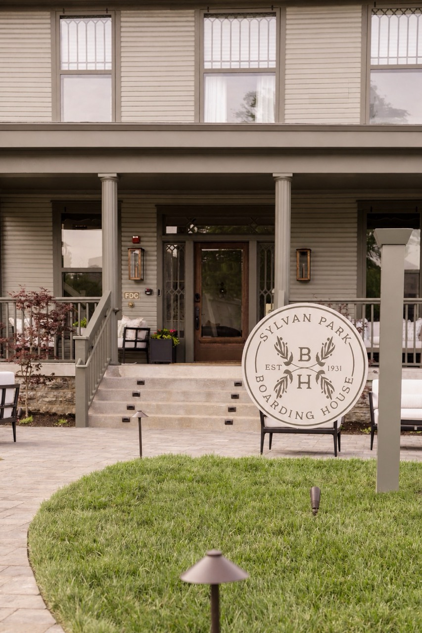 Front view of Sylvan Park Boarding House with a round sign on the lawn and a porch with columns and stairs.