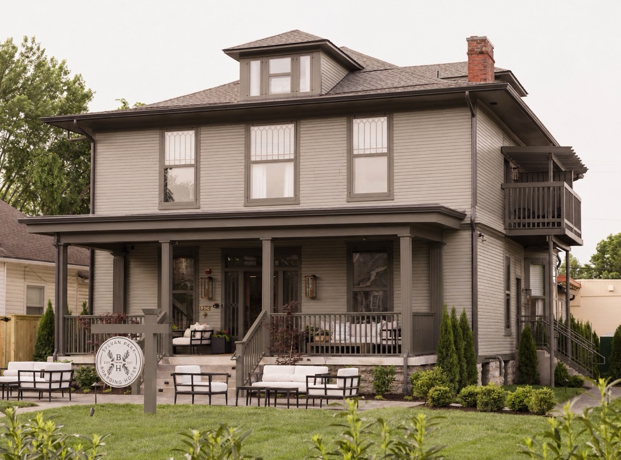 Gray two-story boarding house with porch seating and a sign reading Sylvan Park Boarding House.