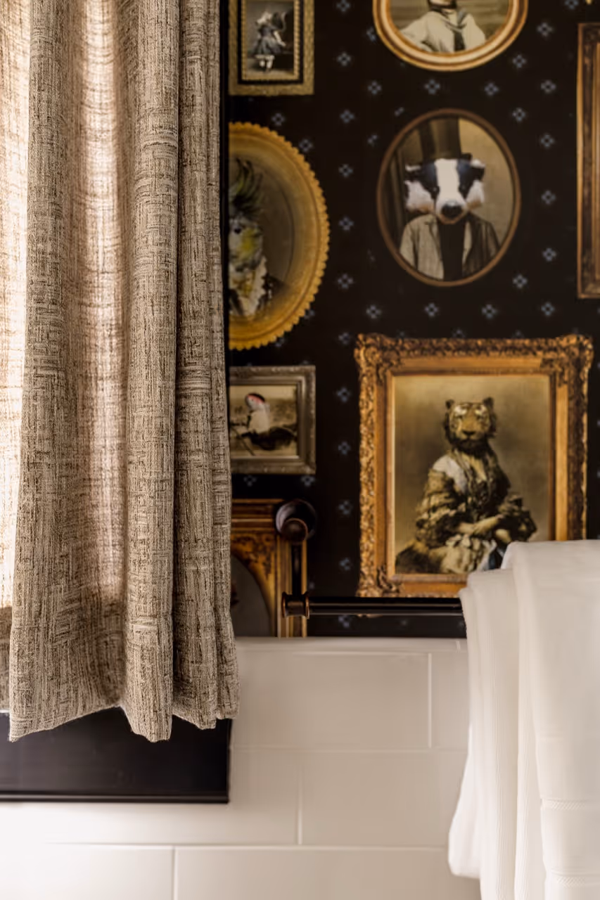 Bathroom wall with wallpaper featuring framed animal portraits and beige textured shower curtain.