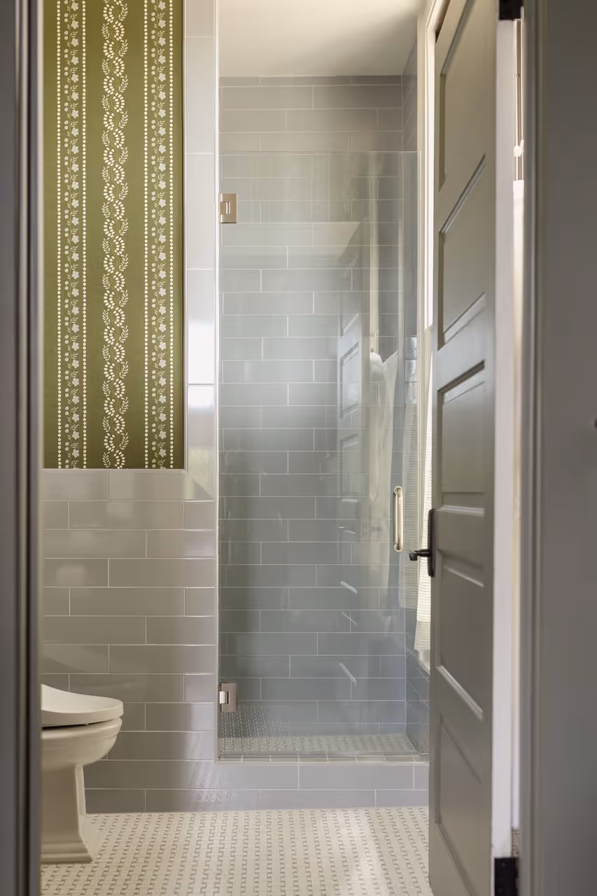 Modern bathroom with gray tiled shower, glass door, patterned floor, and white toilet partially visible.
