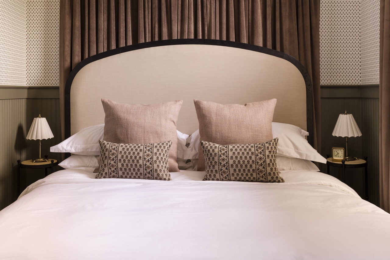 Bed with beige curved headboard, white bedding, neutral pillows, and matching bedside lamps.