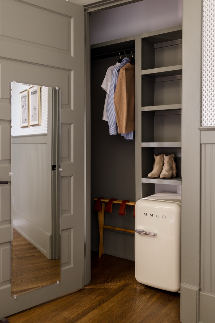 Small closet with hanging shirts, shelves holding boots, a shoe rack, and a SMEG mini fridge.