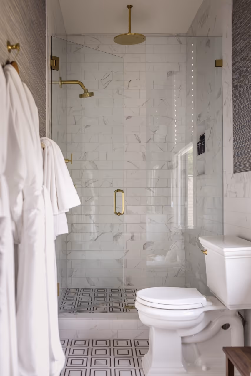 Modern bathroom with white tiled walk-in shower featuring gold fixtures and patterned floor tiles.