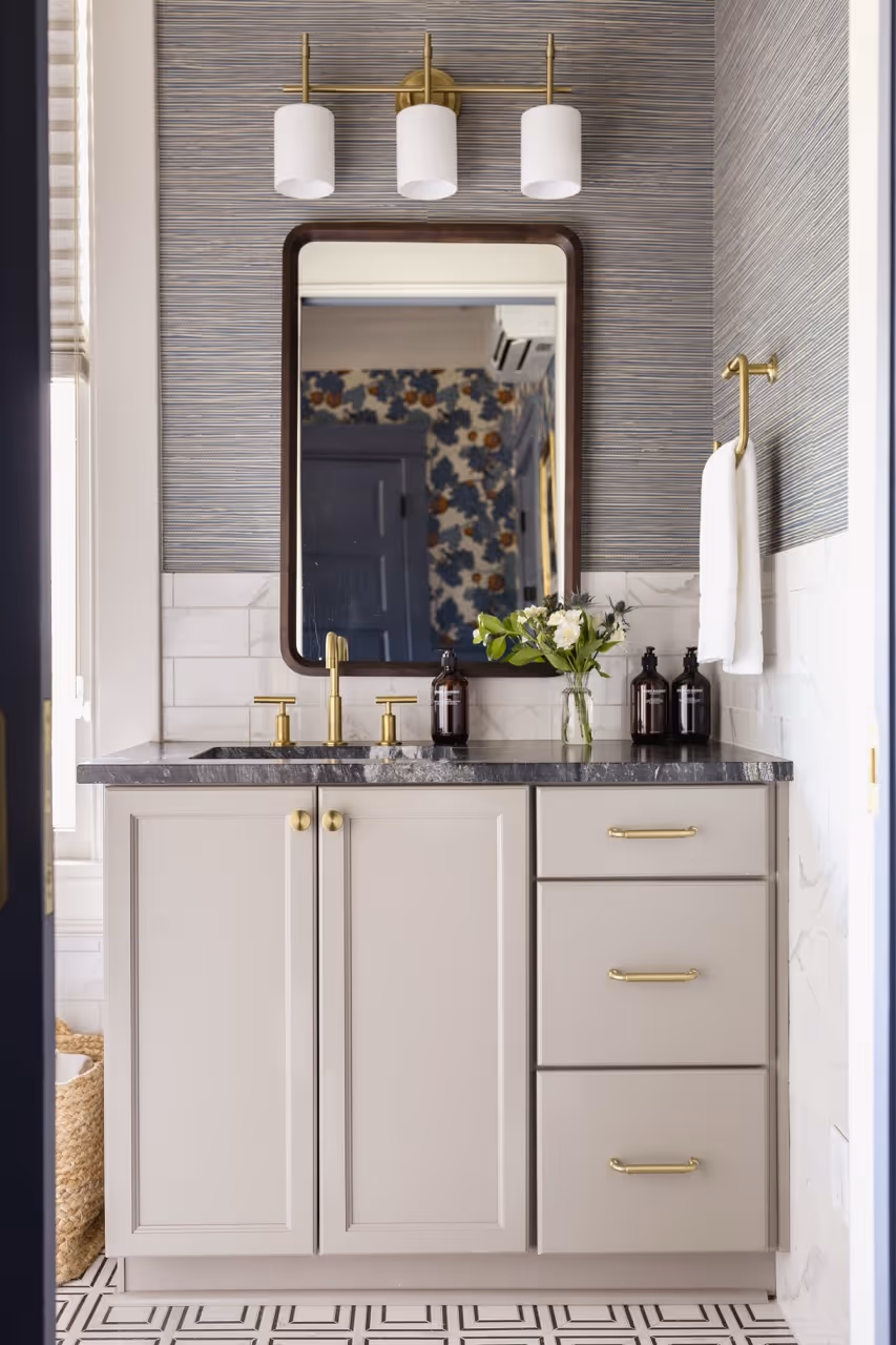 Modern bathroom vanity with beige cabinets, black marble countertop, gold fixtures, and a rectangular mirror.