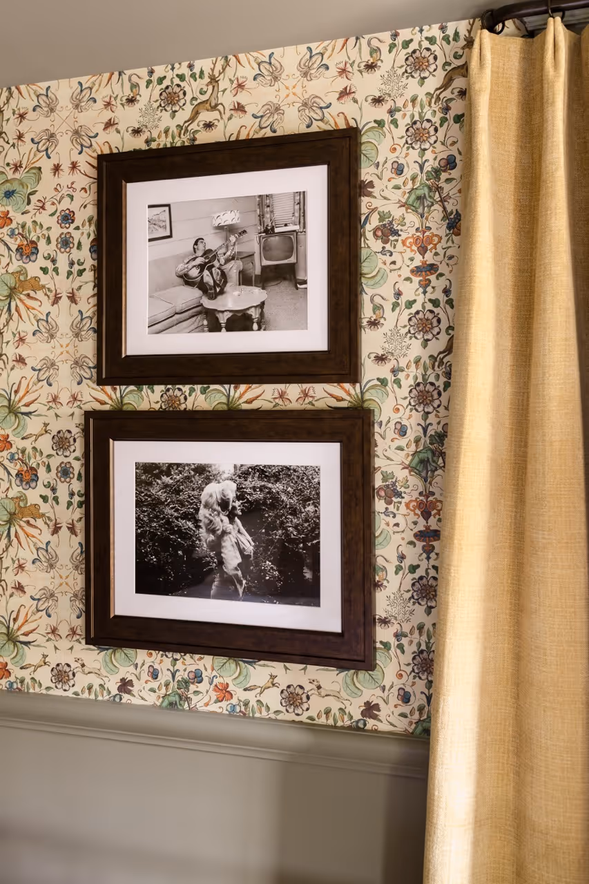 Two framed black and white photos on floral wallpaper beside beige curtains.