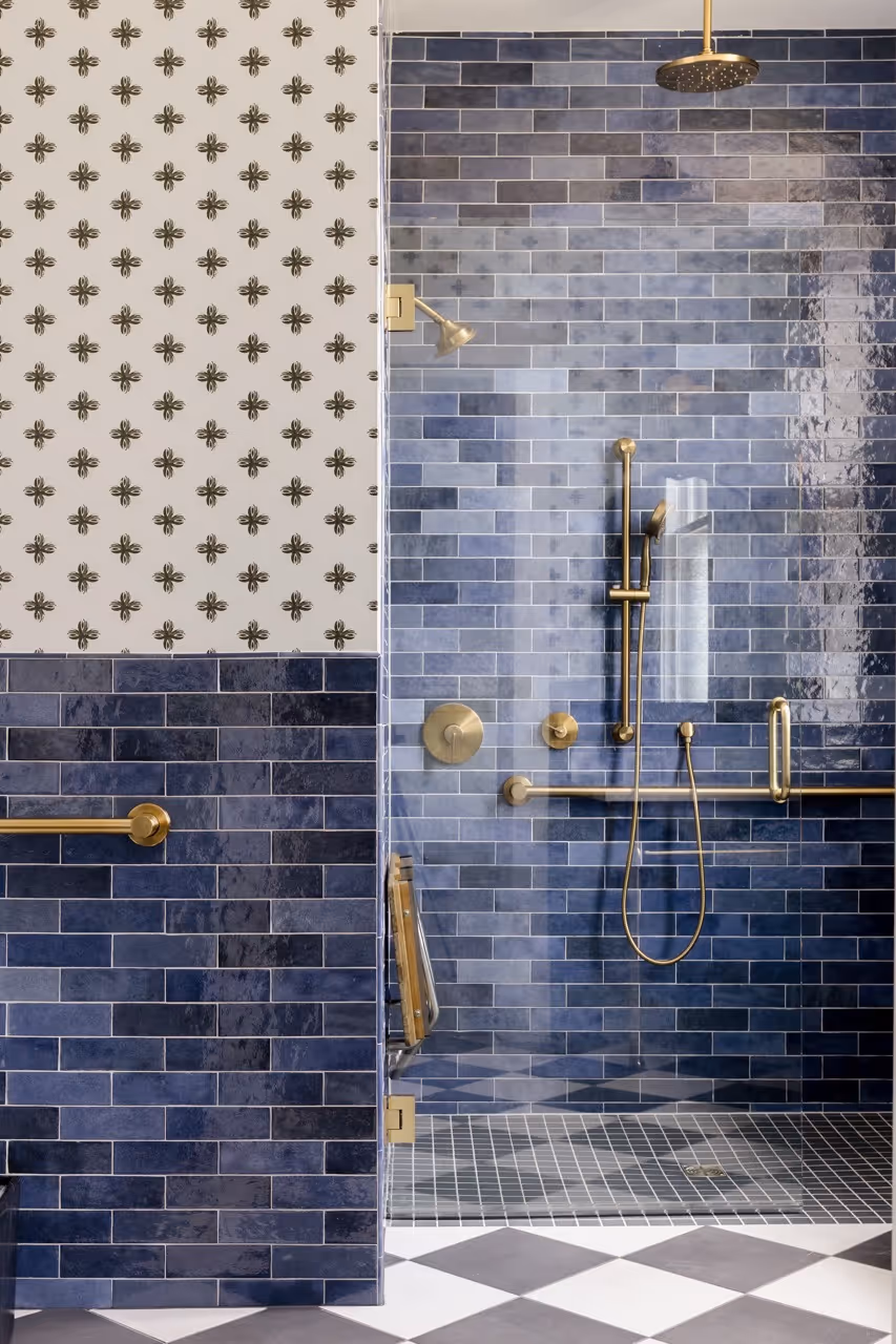 Modern shower with glossy blue subway tiles and gold fixtures inside a glass enclosure.
