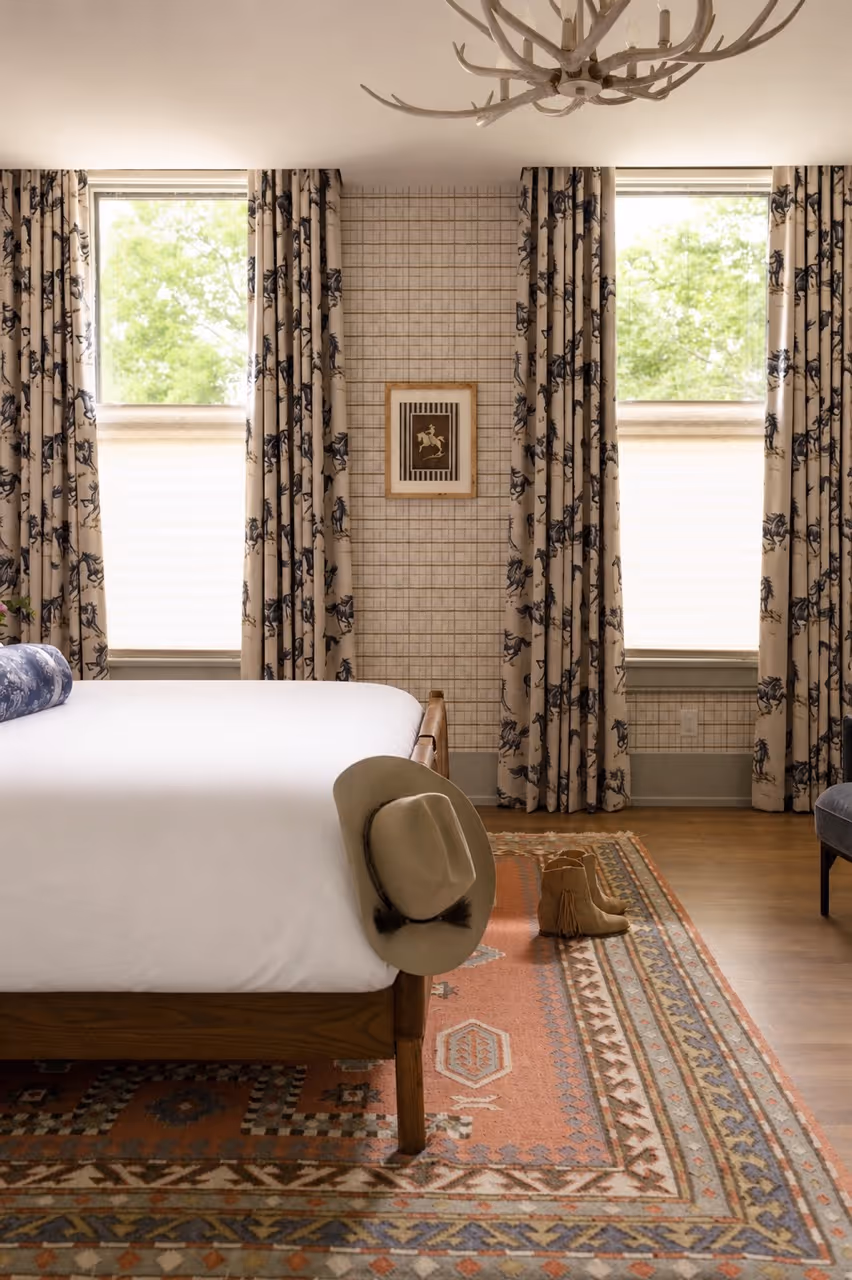 Bedroom with white bed, cowboy hat on bedpost, Native American pattern rug, and horse-themed curtains.