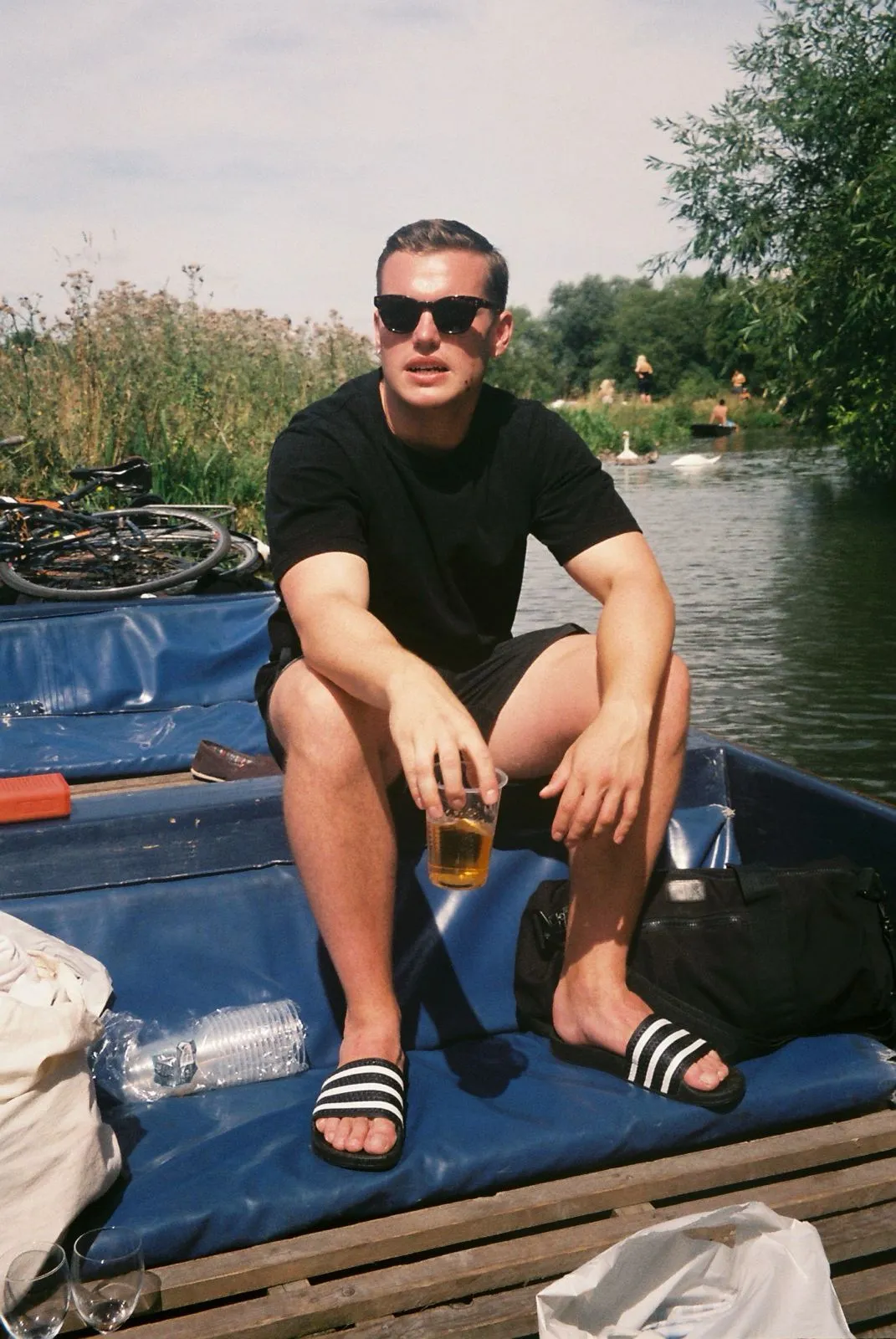 Jack Merritt sitting outdoors by water wearing sunglasses and a black t-shirt