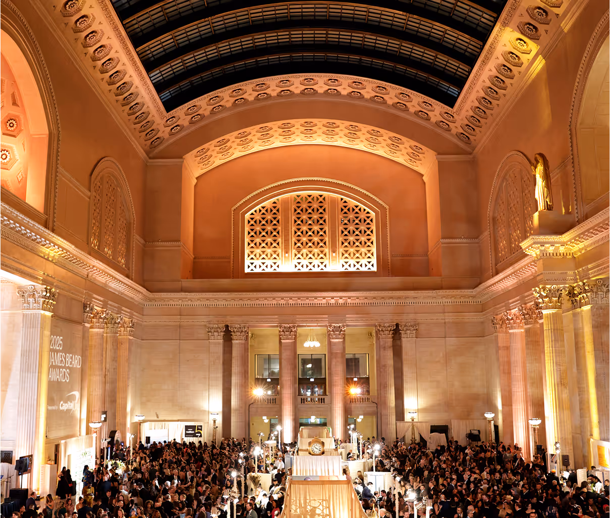 A large crowd gathers in an ornate hall with high arched ceilings, elegant columns, and warm lighting for the 2023 ALMAs Media Awards. The décor is grand and classical, with event signage visible on one wall.