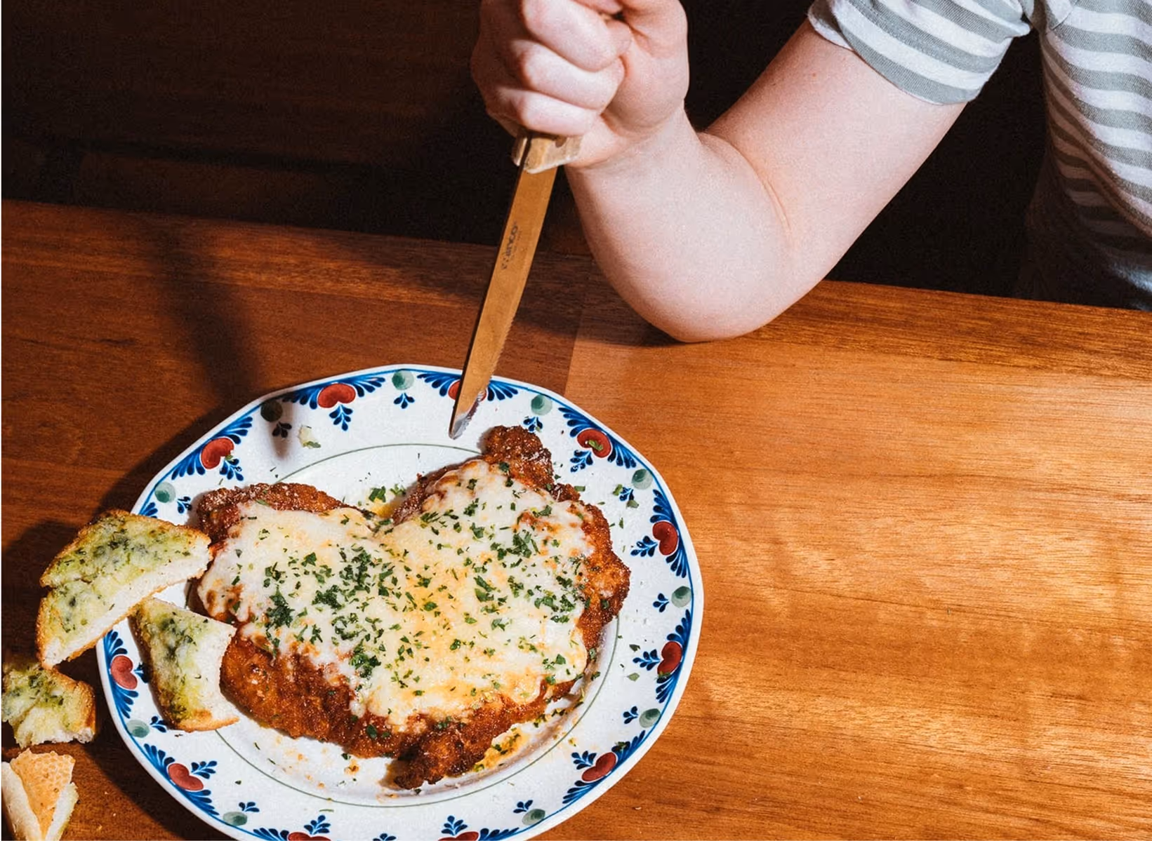 A plate with partially eaten breaded chicken covered in tomato sauce and melted cheese, two forks, and an empty ramekin with sauce residue, all on a wooden table.