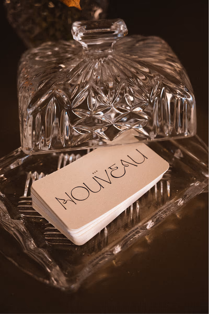 Stack of Bar Nouveau business cards resting in a decorative glass dish with a matching lid.