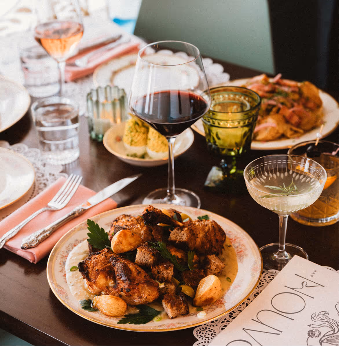 Plate of roasted chicken with garlic and herbs on a table set with wine glasses, deviled eggs, and vintage-style glassware.
