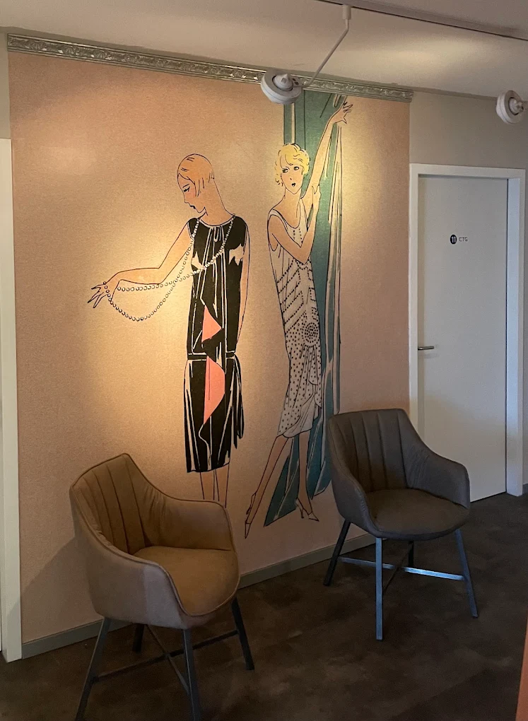 Two modern chairs in front of a wall mural depicting two elegant women in 1920s-style dresses.