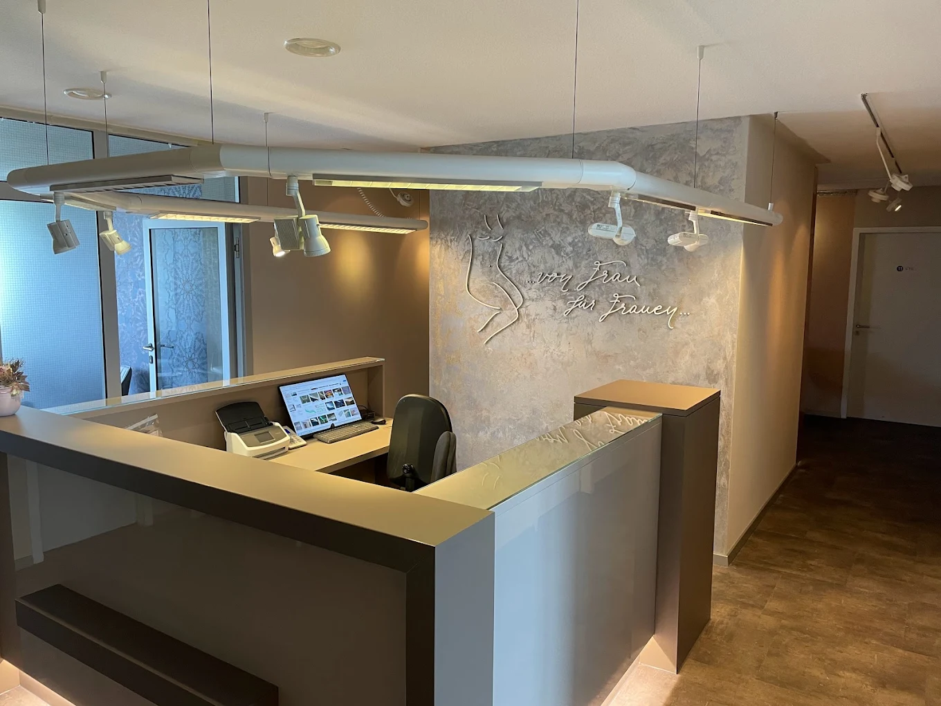 Modern reception desk area with computer, scanner, and wall decoration featuring cursive text and abstract female figure.