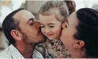 Parents kissing a little girl on the cheek.