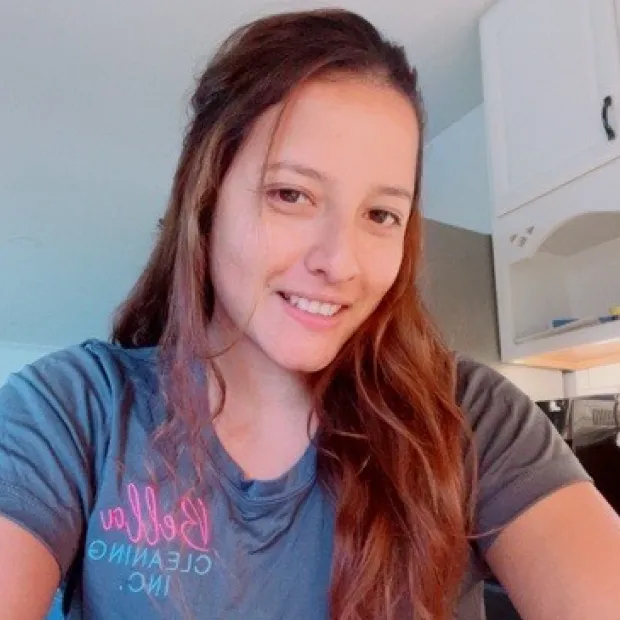 Smiling woman with long brown hair wearing a gray shirt in a kitchen setting.