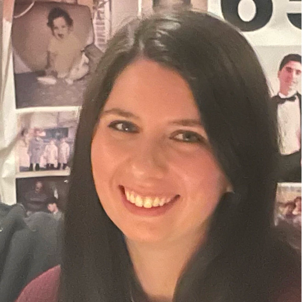 Smiling woman with long dark hair in front of a wall with various photos.