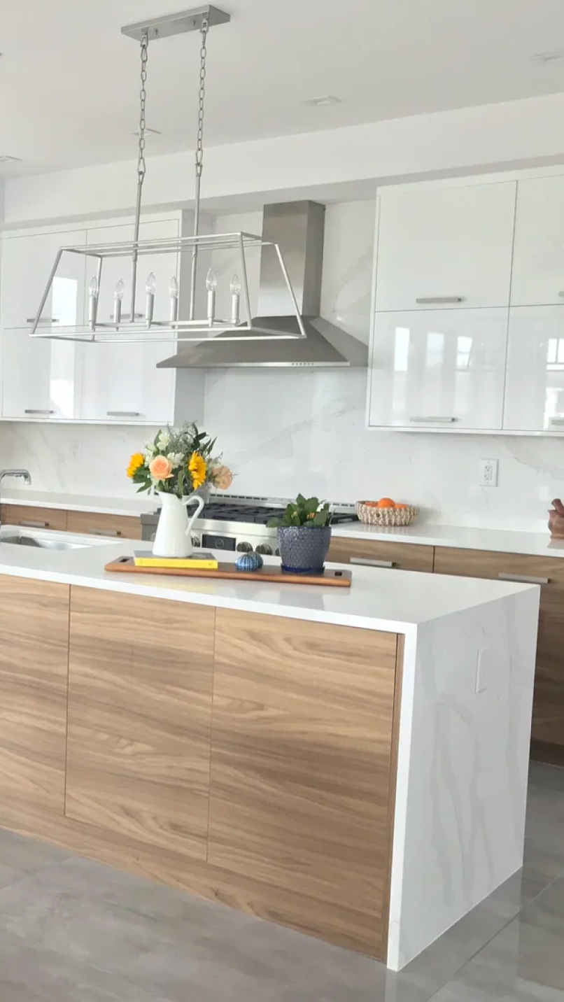 Modern kitchen with white countertops, wood cabinets, a metal chandelier, and floral decor on the island.
