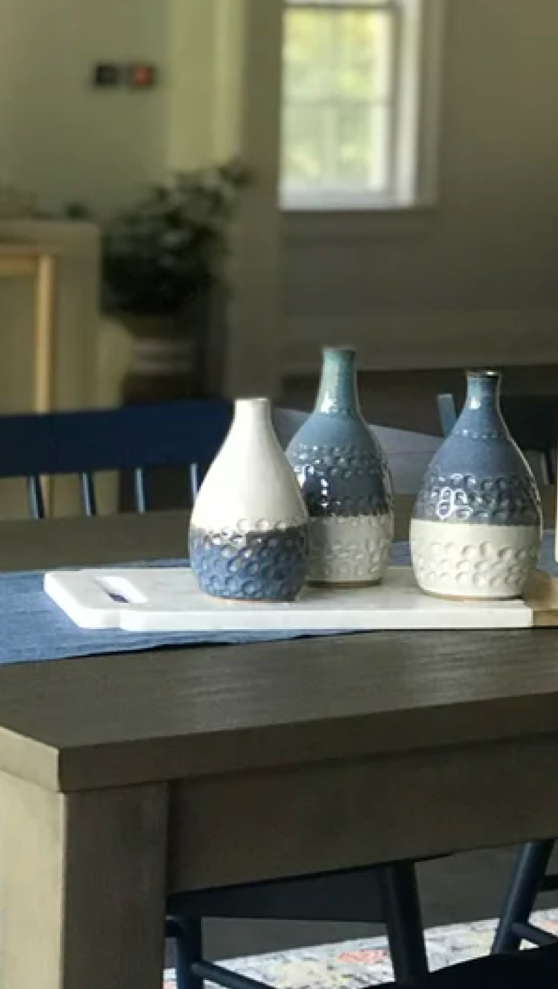 Three decorative blue and white ceramic vases on a white tray on a wooden dining table.