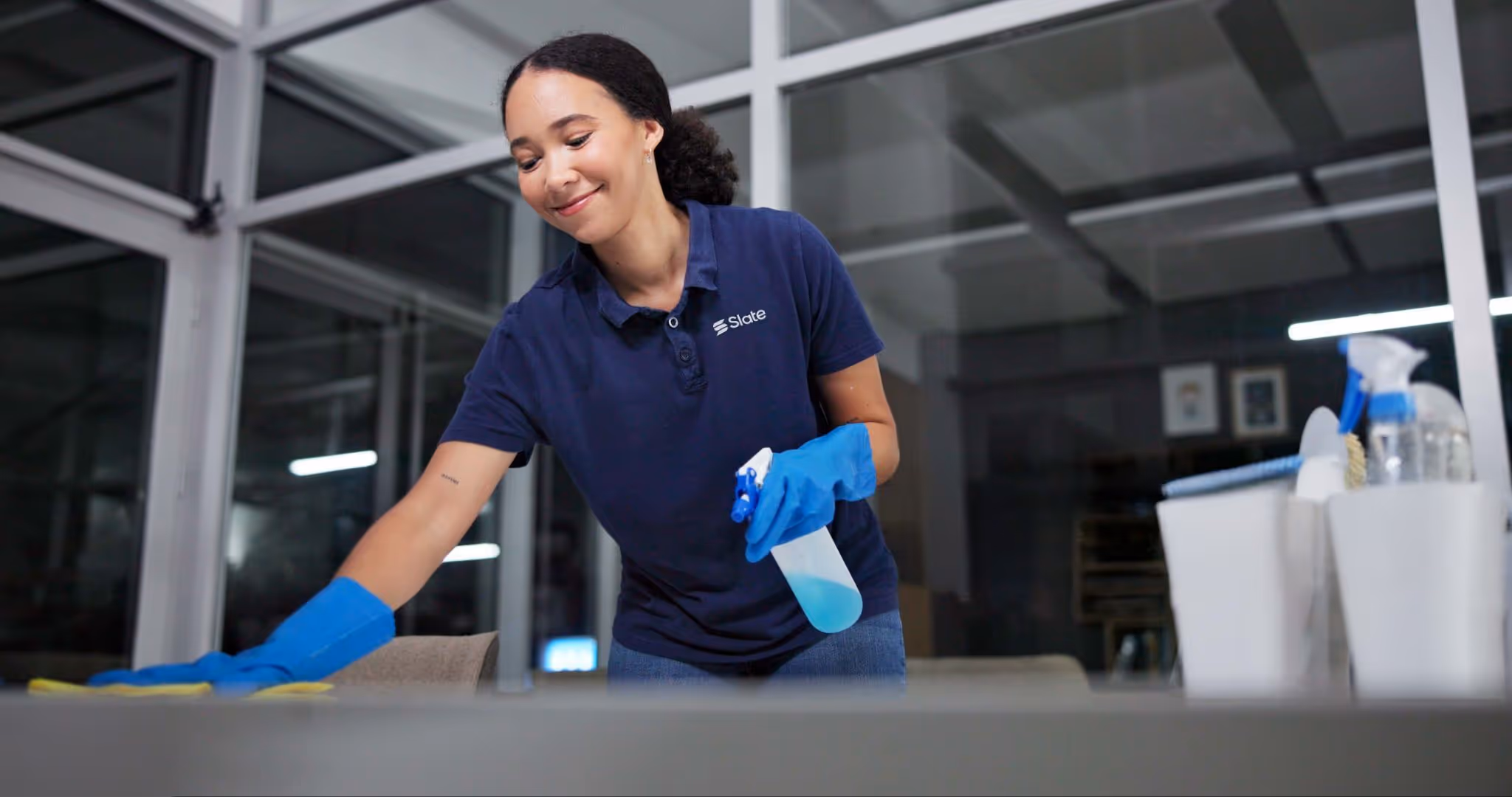 A woman in a blue shirt and blue gloves cleaning a table.