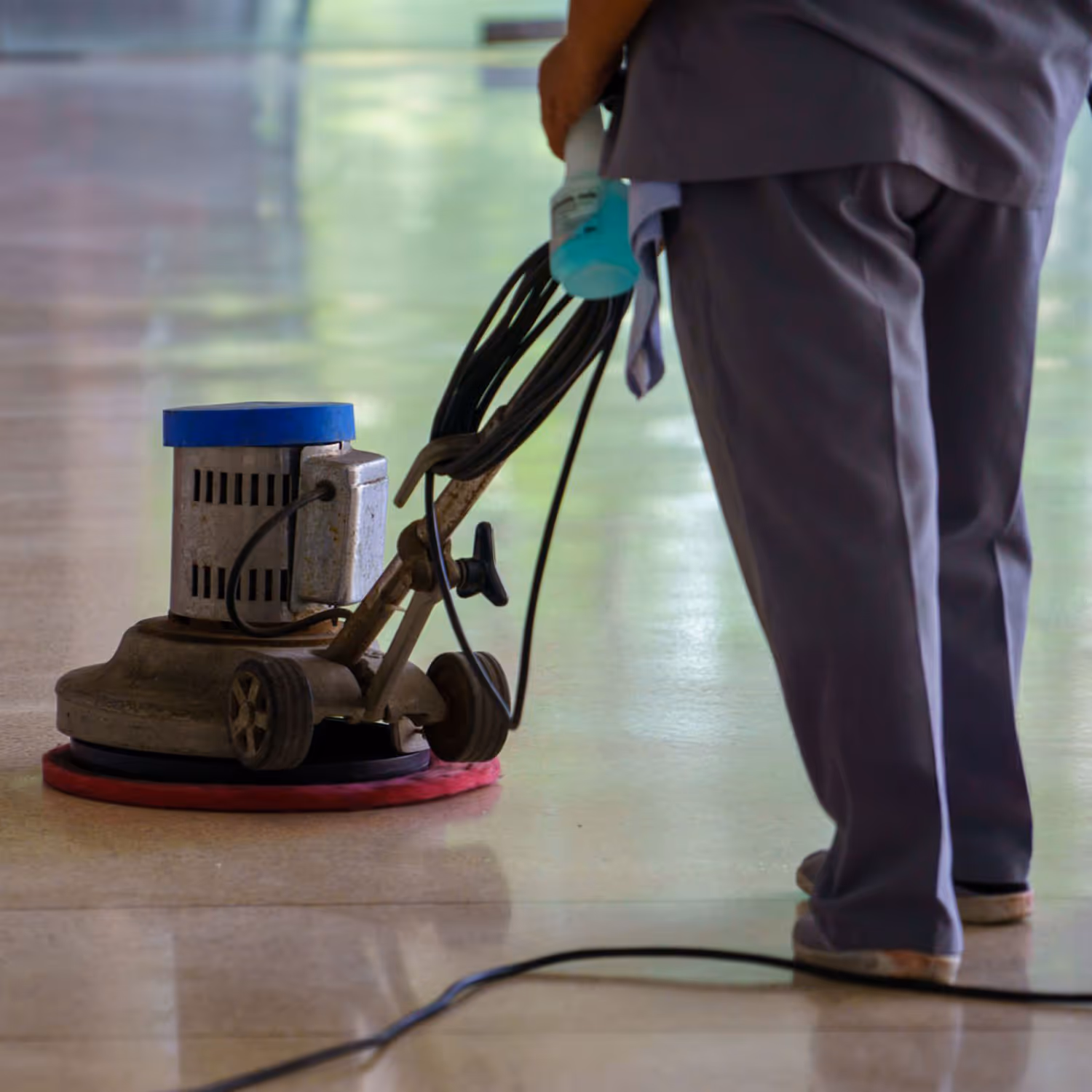 Person operating a floor polishing machine on a shiny tiled surface.