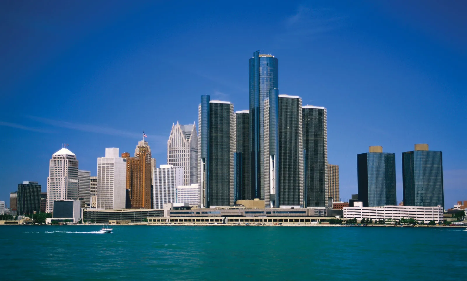 Detroit skyline featuring tall, modern skyscrapers along the waterfront under a clear blue sky. The water is calm, and the scene feels peaceful.
