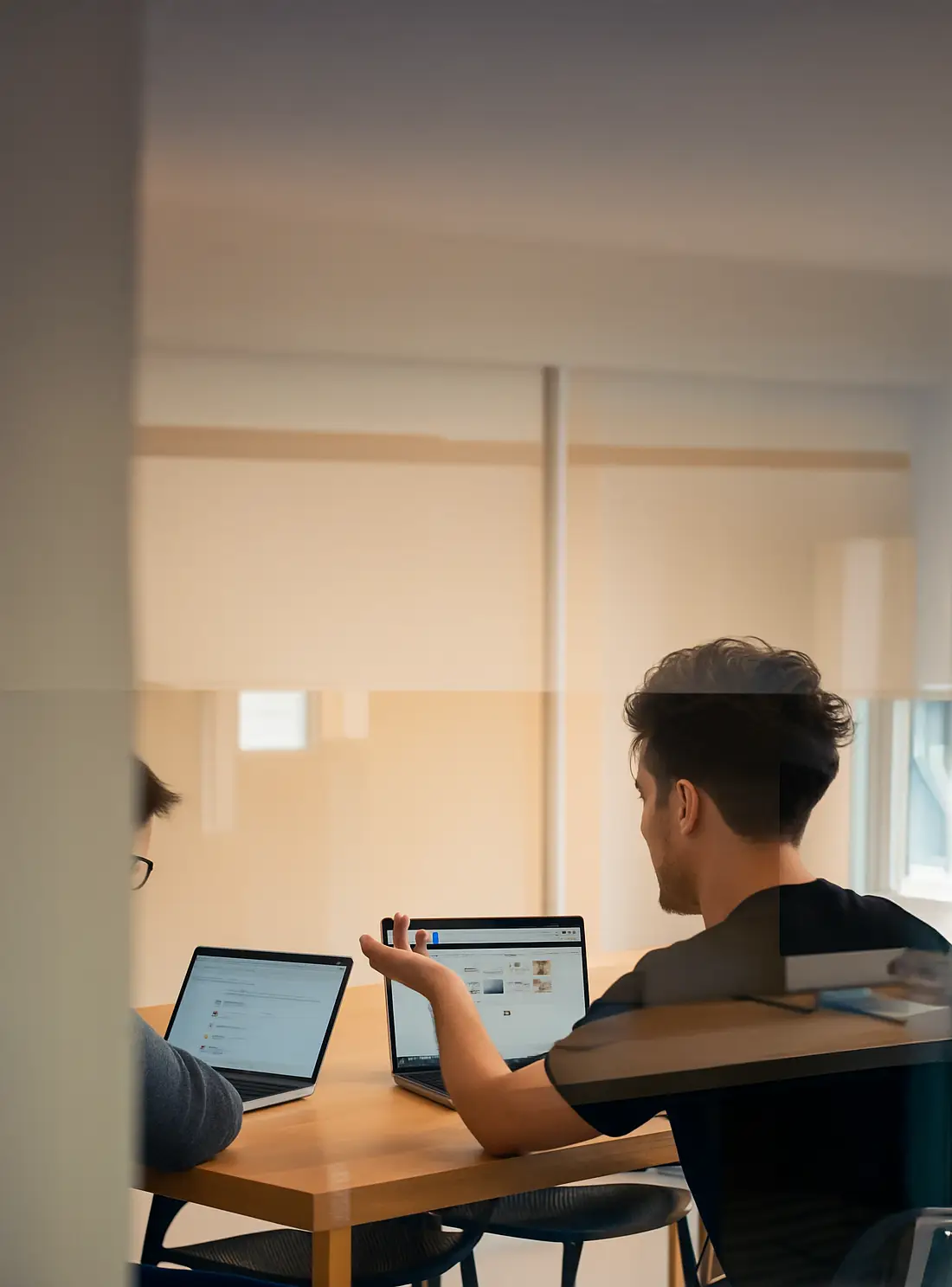Zwei Personen im Meeting mit Laptops – modernes Arbeiten im Büro, Austausch über digitale Projekte und Online-Marketing.