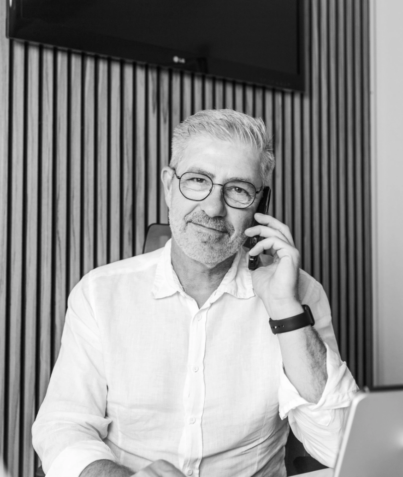 Älterer Mann mit Brille und weißem Hemd spricht am Telefon in modernem Büro.