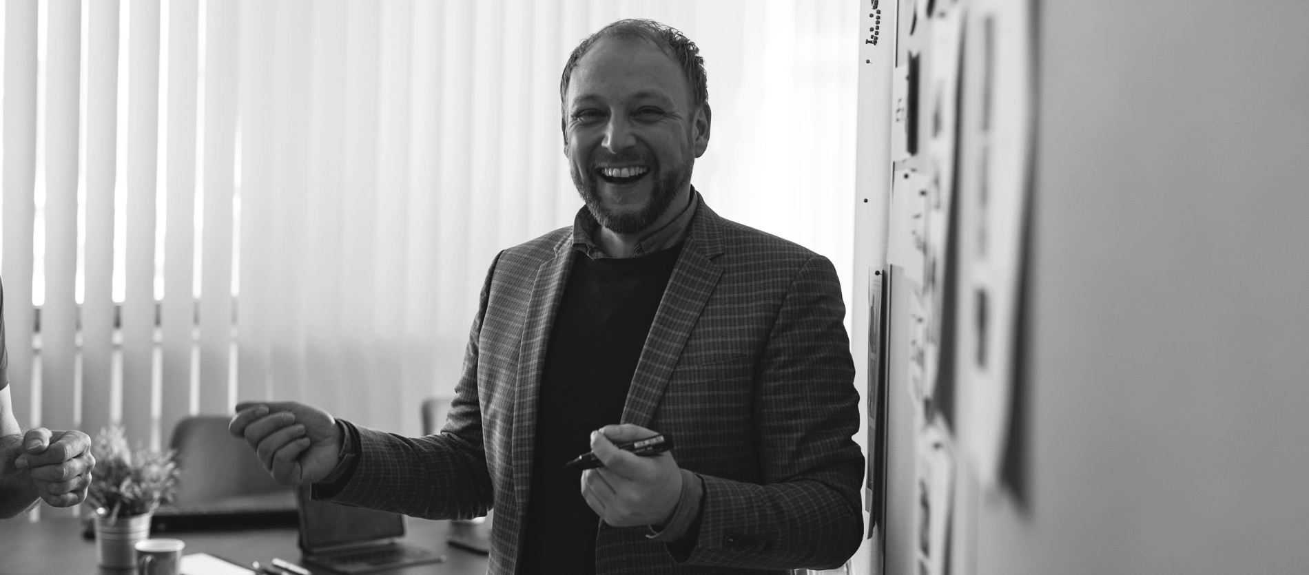 Mann lächelt und hält Marker vor einer Wand mit Fotos und Notizen in einem Büro.