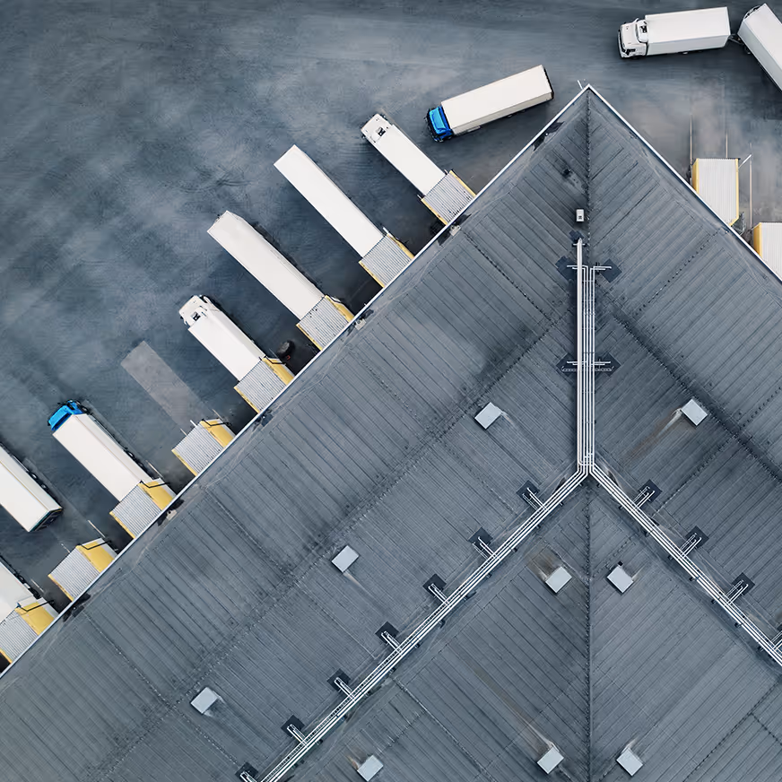 Drohnenaufnahme eines Lagers mit mehreren angelandeten LKWs an Verladerampen.