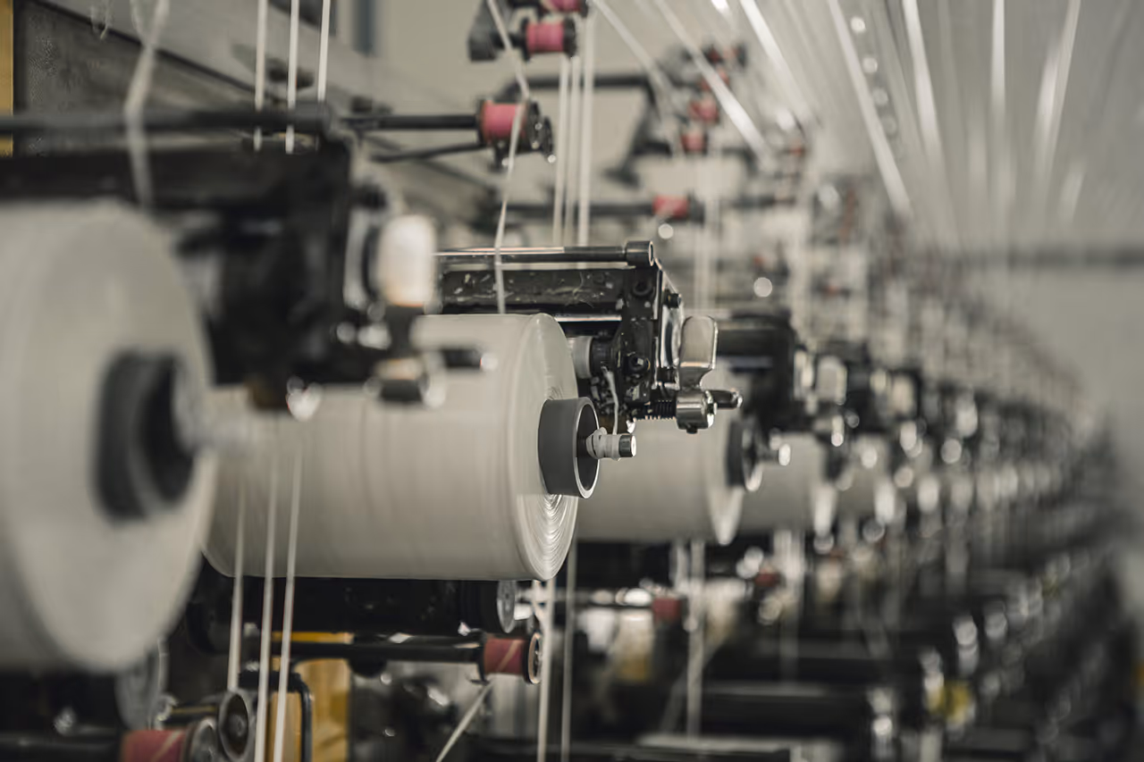 Reihe von Maschinen mit großen Garnrollen in einer Textilfabrik.