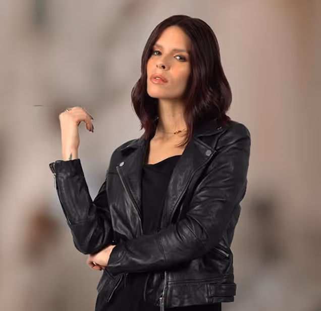 Femme aux cheveux auburn portant une veste en cuir noire et une robe noire, posant avec une expression confiante.