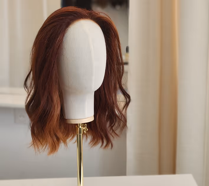 Perruque brune ondulée sur un mannequin en tissu beige avec un support en métal doré.