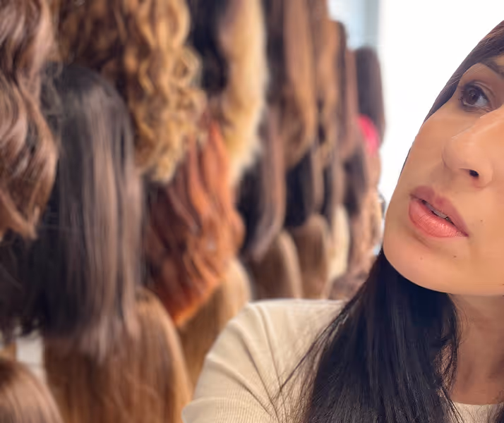 Femme examinant différentes perruques suspendues dans un magasin de coiffure.