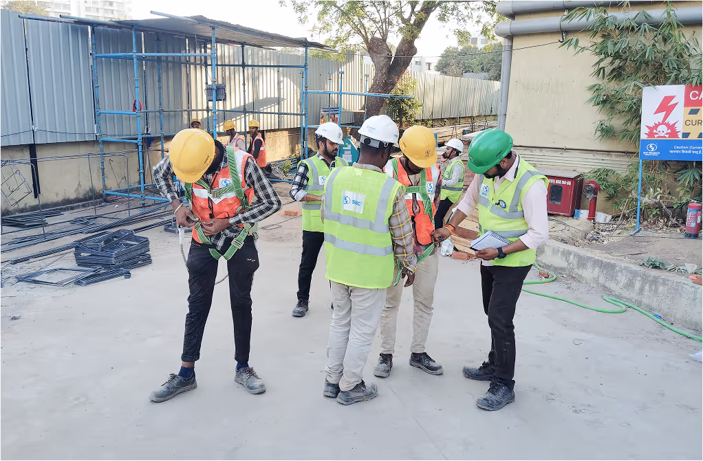Group of construction workers wearing safety helmets and vests inspecting safety harnesses on a construction site.