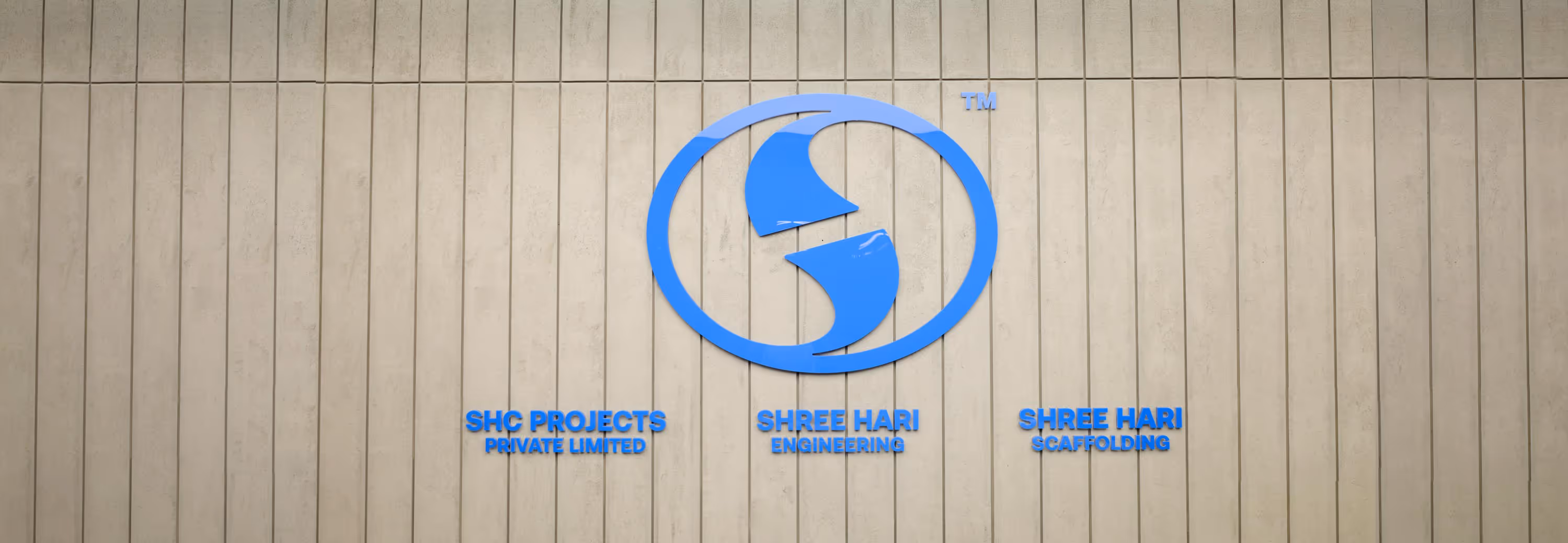 Blue logo with stylized shapes inside a circle above the text 'SHC PROJECTS PRIVATE LIMITED,' 'SHREE HARI ENGINEERING,' and 'SHREE HARI SCAFFOLDING' on a beige tiled wall.