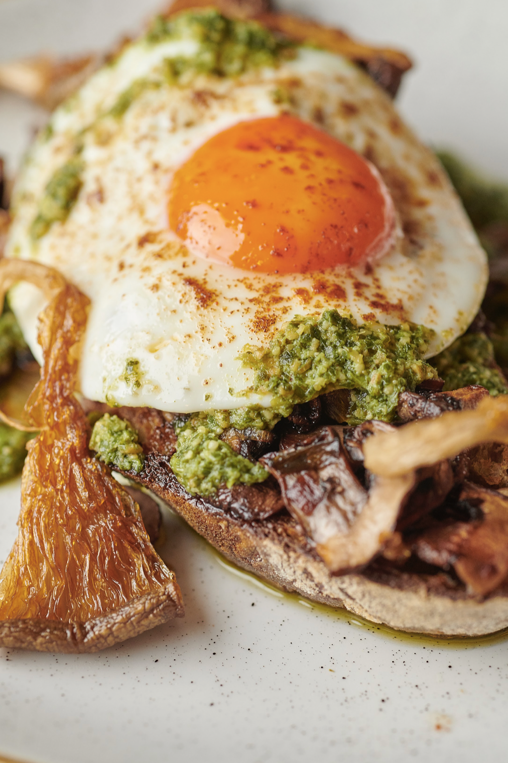 Fried egg with runny yolk on toast topped with mushrooms and green herb sauce on a plate.