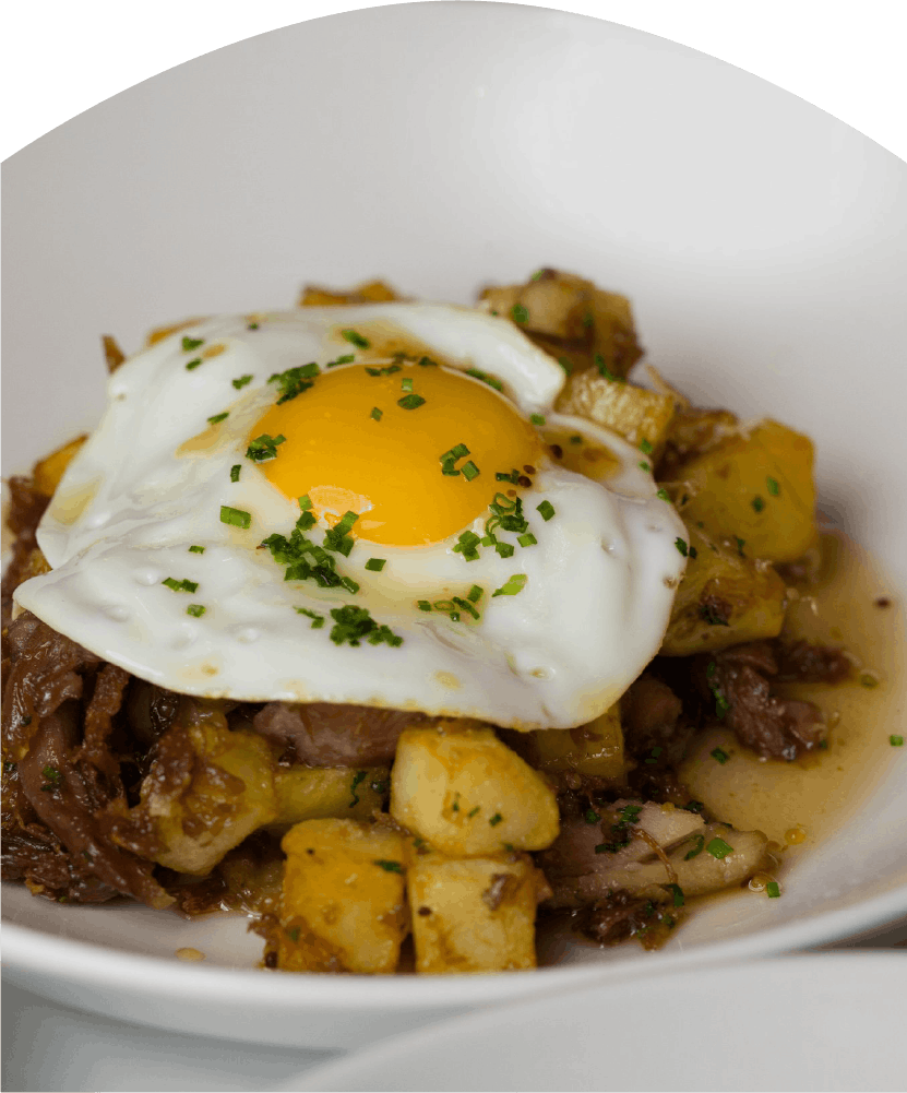Fried cubed potatoes and shredded meat topped with a sunny-side-up egg garnished with chopped herbs.