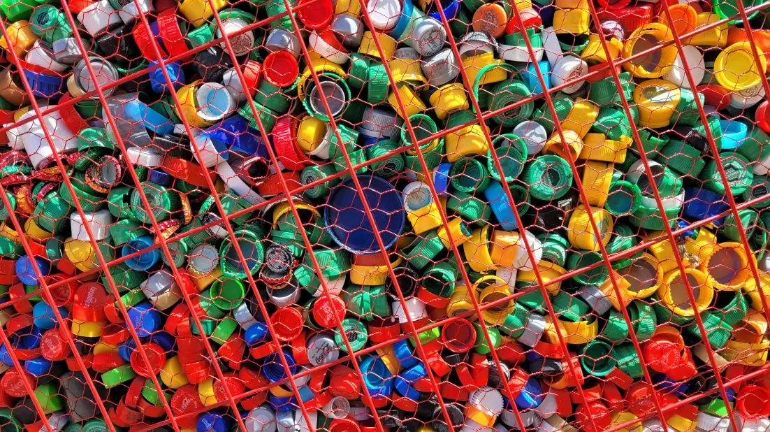 Colorful plastic bottle caps collected in a red wire mesh container, symbolizing recycling efforts and sustainable waste management practices.