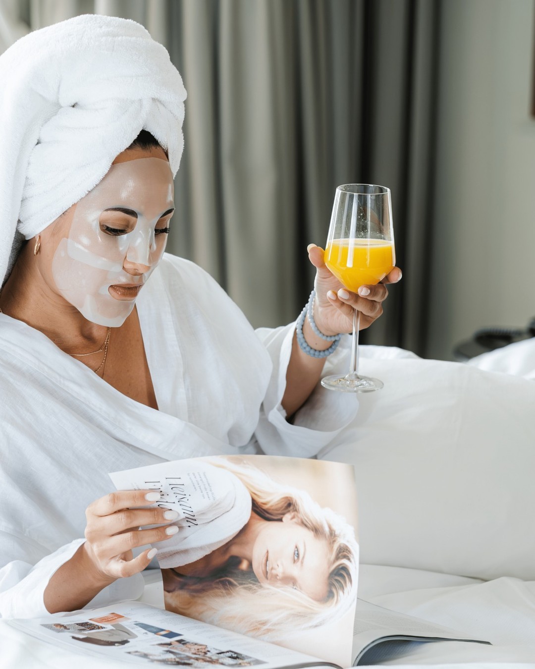 Femme se reposant avec son soin visage Gemology tout en sirotant un jus d'orange et lisant un magazine de mode